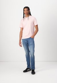 Camiseta de manga corta rosa claro, combinada con vaqueros de denim azules y zapatillas deportivas negras. El diseño es casual y ajustado.