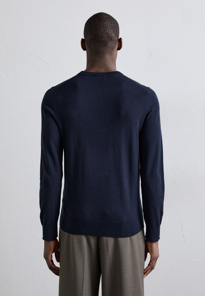 Jersey de punto azul marino, cuello redondo, mangas largas, tejido texturizado, acabado suave, dobladillo ajustado, combinado con pantalones grises claros.