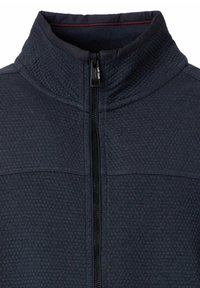 Marineblauwe fleecjas met een hoge kraag, gestructureerd oppervlak, ritssluiting aan de voorkant en contrasterende rode stiksels langs de kraag.