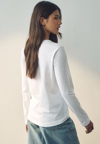 Camicia bianca a maniche lunghe in cotone leggero, abbinata a jeans azzurri chiari. Presenta un collo rotondo semplice e una vestibilità comoda.