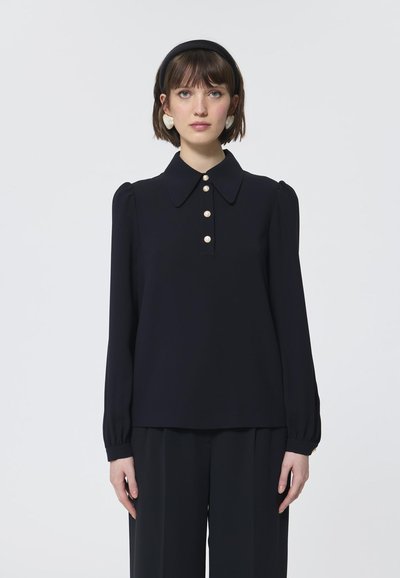 Blouse noire à manches longues avec un grand col et trois gros boutons en perles à l'avant, présentant des détails froncés aux épaules. Tissu lisse.