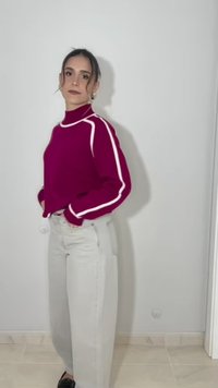 Femme debout à l'intérieur portant un pull magenta à rayures blanches et un pantalon gris clair taille haute, regardant la caméra avec confiance.