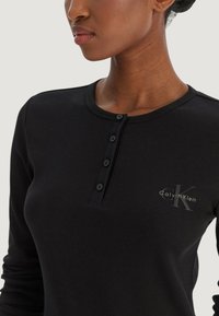 Czarna prążkowana bluzka z długim rękawem, okrągłym dekoltem, czterema guzikami oraz subtelnym nadrukiem z logo "Calvin Klein" na piersi.