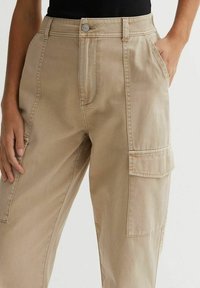 Beige cargobroek met een relaxte fit, voorzien van zijzakken, voorplooien, een knoopsluiting en subtiele stikseldetails.