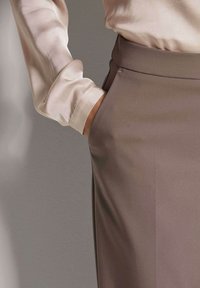 Beige satijnen blouse met lange mouwen, gecombineerd met een soepel taupekleurige rok met een zijzak en strakke, verzorgde lijnen.