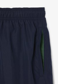 Pantaloni corti blu navy con cintura elastica, tasche laterali con rifinitura verde e una texture di tessuto liscia e leggera.