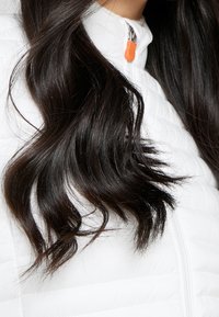 White puffer jacket with a high collar, featuring a zip closure and orange zipper pull. Textured surface and stitched pattern visible.