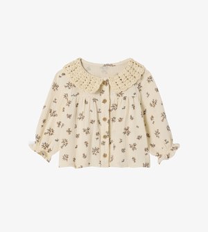 Cream blouse with floral print in blue and brown, featuring a crochet collar, button closure, and gathered sleeves. Lightweight, textured fabric.