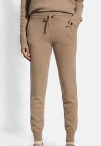 Joggers de punto beige con cintura ajustable, puños acanalados y bolsillos laterales, elaborados en un tejido suave y texturizado.