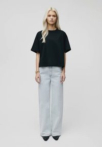Svart kortermet crop top kombinert med lyseblå vide jeans og svarte spisse hæler, med en jevn tekstur og minimalistisk design.
