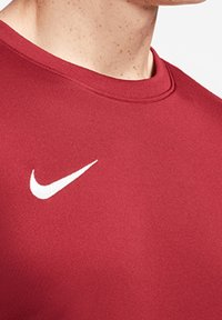 Red athletic shirt with short sleeves, a crew neck, and a white Nike swoosh logo on the left chest area. Smooth fabric texture.