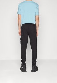 Ljusblå kortärmad skjorta i kombination med svarta cargobyxor med sidofickor, slät textur och elastisk midja, kompletterat med svarta sneakers.