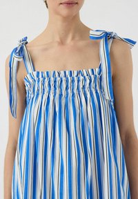 Stropeløs kjole med lodrette blå og hvide striber, featuring en smocket bodice og sløjfebånd på skulderstropperne. Letvægts stoftekstur.