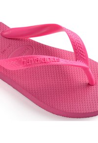 Rózsaszín gumi papucs, texturált felülettel. Vékony pántokkal és formázott talppal rendelkezik. A márka logója, a „havaianas” a talpba van gravírozva.
