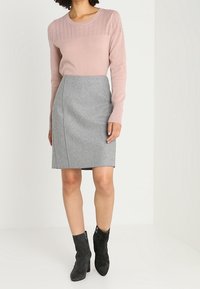 Ljusrosa tröja med texturerad stickning, i kombination med en grå midikjol. Modellen bär svarta ankelskor med sidodragkedjor.