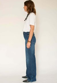 Jean skinny bleu foncé à taille haute et coupe droite, associé à un t-shirt blanc ajusté et des ballerines noires pointues.