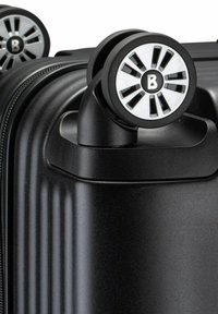 Ecke eines schwarzen Hartschalenkoffers mit Doppel-Spinnerrädern mit silbernen Akzenten und einem Reißverschluss an der Seite.