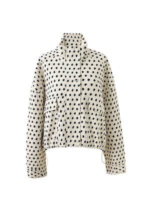 Witte fleecejas met zwarte onregelmatige polka dots, hoge kraag, drukknoopsluiting, voorzakken en lange mouwen, geïsoleerd op een witte achtergrond.