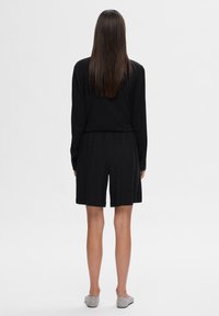 Haut noir à manches longues associé à des shorts noir jusqu'aux genoux, avec une coupe décontractée et une taille élastique, vu de dos.