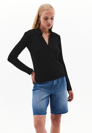 Mustassa pitkähihaisessa polo-paidassa on kaulus, ja se on yhdistetty vaaleansinisiin farkkushortseihin, joissa on kuluneet reunat. Yksinkertainen, istuva malli.