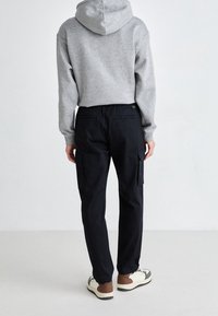 Gray hooded sweatshirt with a relaxed fit paired with black cargo pants featuring multiple pockets, and white sneakers with brown accents.