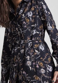 Mörk blommig skjortklänning med figursydd midja, långa ärmar och knapprad. Materialet har en mjuk textur med flerfärgade blommönster.