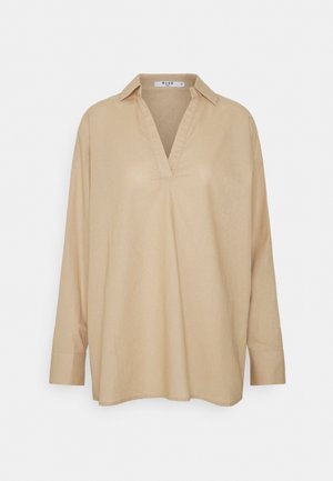 Béžová košile s dlouhým rukávem a límečkem, která má véčkový výstřih a volný střih. Vyrobená z lehké látky s hladkou texturou.