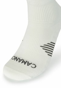 Hvide sportsstrømper lavet af et tekstureret stof, med et sort logo og vandrette striber nær anklen for ekstra detaljer.