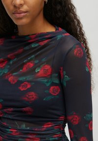 Langärmlige Bluse aus durchsichtigem Marineblau mit floralen Mustern, die rote Rosen und grüne Blätter zeigt, und mit Raffung an den Seiten.