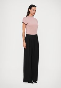 Top ajustado rosa claro de manga corta, combinado con pantalones de pierna ancha negros de cintura alta, llevado con zapatos negros de puntera.