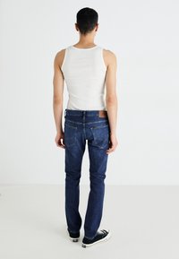 Mørkeblå denimjeans med slim fit, baklommene og en merkevarebelte. Brukt med en hvit tank topp og svarte joggesko.