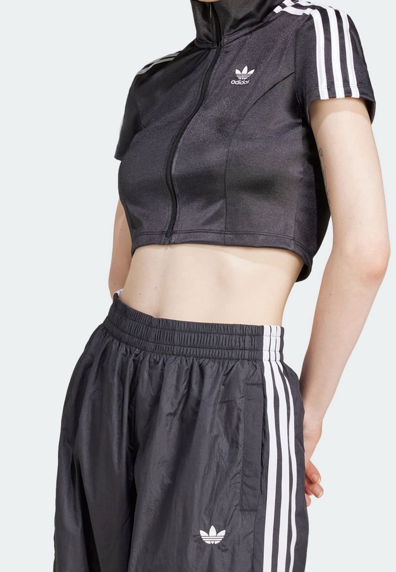 Svart kortärmad zip-up-jacka med vita ränder, kombinerad med matchande svarta joggers med elastisk midja och logotyp.