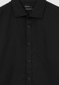 Schwarze Hemdjacke aus strukturiertem Stoff, mit Kragen, sechs Knöpfen und einem Etikett, das "CALLIOPE" anzeigt, Größe L, normale Passform.