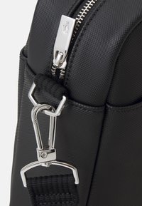 Schwarze strukturierte Stofftasche mit einem silbernen Reißverschluss und Hardware, einem stabilen Clip und einem gewobenen Riemen-Detail. Nahaufnahme der Designelemente.