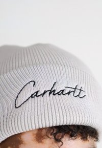 Graue gestrickte Mütze mit gerippter Textur, auf der Vorderseite mit schwarzem gesticktem "Carhartt"-Logo. Einfaches und funktionales Design.