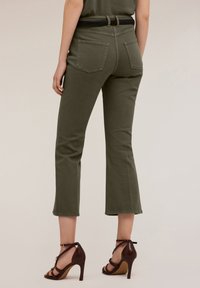 Olivgrön cropped byxor med en åtsittande midja och bakfickor. Bärs med bruna högklackade sandaler med ankelremmar. Slät textur.