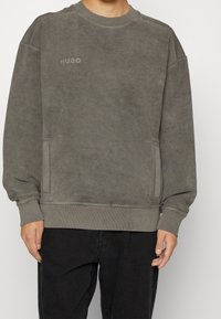Sweat-shirt gris en tissu doux, avec un col rond, des poignets côtelés et des poches latérales. Logo "HUGO" brodé sur la poitrine.