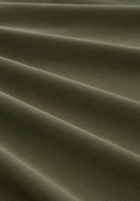 Olivgrüner, strukturierter Stoff mit sichtbaren horizontalen Falten, hergestellt aus einem strapazierfähigen Material, das eine glatte Oberfläche und ein dezentes Webmuster aufweist.