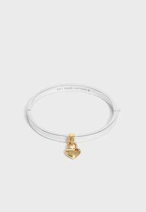 Bracelet jonc en argent avec un petit pendentif en forme de cadenas cœur doré suspendu dessus sur un fond blanc.