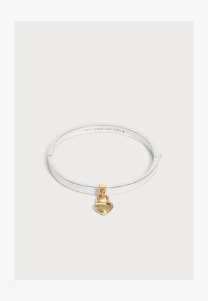 Bracelet jonc en argent avec un petit pendentif en forme de cadenas cœur doré suspendu dessus sur un fond blanc.