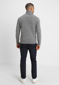 Suéter gris de punto con cuello alto, patrón texturizado y dobladillo acanalado. Combinado con pantalones oscuros y zapatillas blancas.