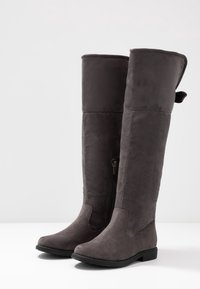 Šedé kozačky nad kolena z měkké semišové kůže, s bočním zipem, plochou podrážkou a očkem na horním okraji pro snadné nazouvání.