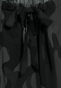 Tessuto di colore nero con motivo camouflage, caratterizzato da una texture morbida e liscia; presenta una vita arricciata con un fiocco legato e cuciture piatte.
