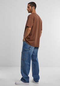 Ruda medvilninė trumpomis rankovėmis marškinėliai, derinami su laisvo stiliaus mėlynais džinsais iš džinsinio audinio, turinčiais kišenes ir pašviesintą tekstūrą. Balti sportbačiai.