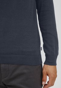 Marineblauer Pullover aus gestricktem Stoff mit gerippten Bündchen und Saum. Verfügt über ein kleines Etikett an der Seite, hat eine glatte Textur und eine taillierte Silhouette.
