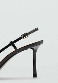 Zwarte sandaal met hoge hak en glanzende afwerking, voorzien van een smalle enkelband met een rechthoekige gouden gesp en een puntige teen.