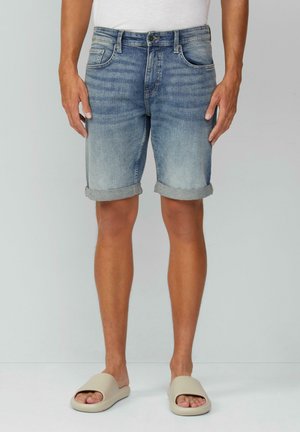 Shorts en denim bleu clair avec une finition délavée, ourlets repliés, design traditionnel à cinq poches et texture usée. Associés à des sandales à glissière beige.