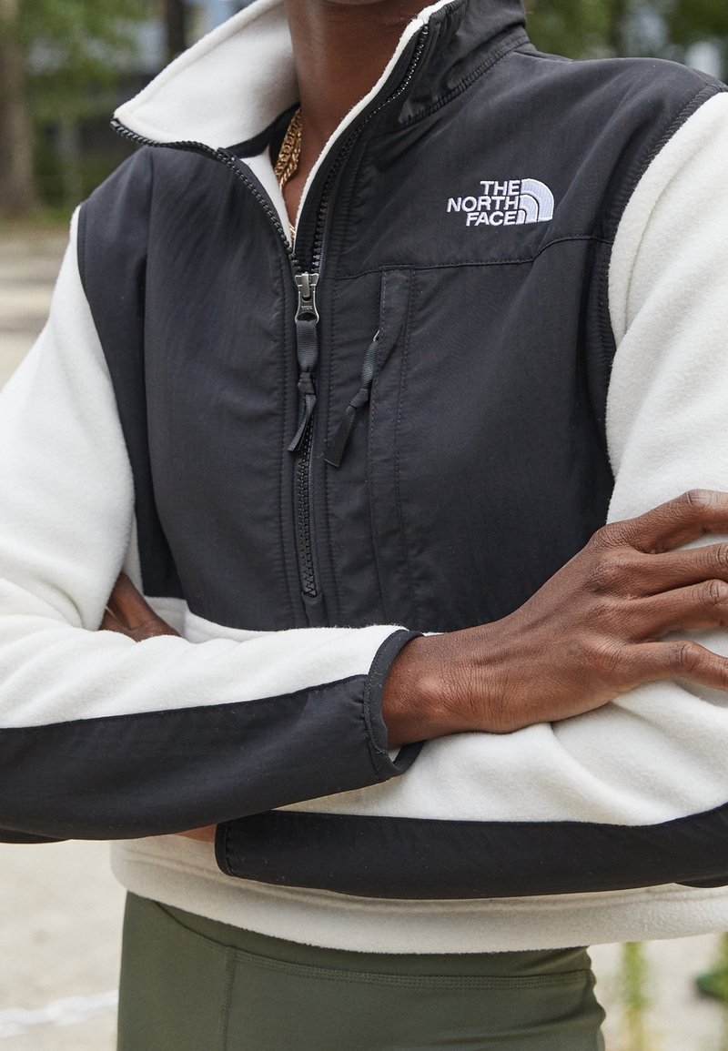 Zwart-witte ritsjacket met fleecetextuur en verstelbare koorden. Heeft een logo op de borst en contrasterende kleuren op de mouwen.