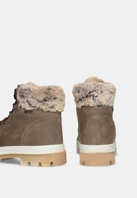 Bottines marron avec col en fausse fourrure, supérieure en cuir texturé, semelle intermédiaire blanche et semelle extérieure en caoutchouc beige, présentant un système de laçage et un détail de logo.