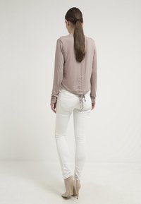 Jasnoróżowa bluzka z długim rękawem z marszczonym detalem z tyłu, zestawiona z białymi obcisłymi dżinsami i cielistymi szpilkami. Gładki materiał i dopasowany krój.